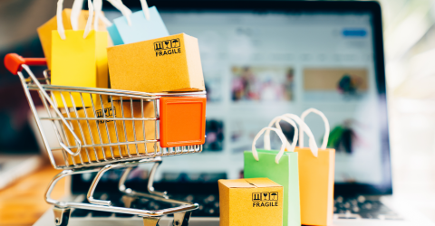 Webshop, online shoppen: laptop met er voor een winkelwagentje met allemaal tasjes erin en ervoor